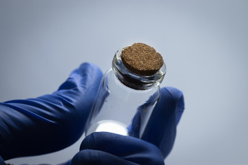 Close-up of a man in blue gloves holding a test tube with a cork stopper