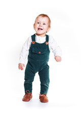 a cute one-year-old child stands in a White Studio. He is dressed in a white shirt and overalls