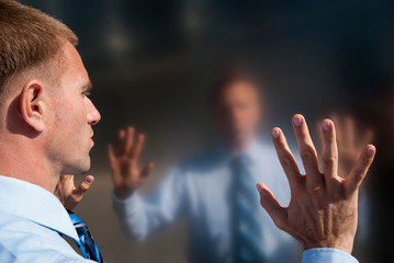 Pensive businessman standing touching his reflection on shiny metal wall