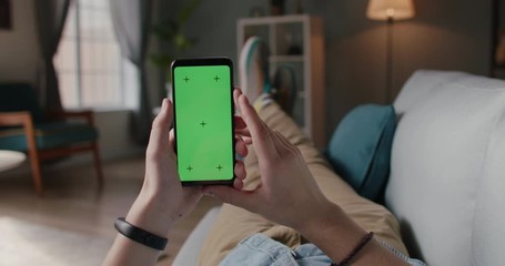 Wall Mural - Close up shot of person relaxing on sofa and using smart phone with mock up green screen, doing various gestures - technology, communication 4k video template