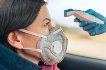 Wall Mural - Temperature check point - the woman behind the wheel of the car in an anti-virus mask is subjected to temperature measurement. Coronavirus concept - restrictions, quarantine, isolation