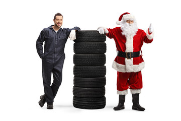 Wall Mural - Auto mechanic and Santa gesturing thumb up and leaning on a pile of tires