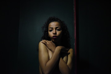 Wall Mural - young naked African woman posing at studio, face with hand portrait over dark background	