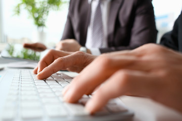 Male arms in suit typing on white keyboard using computer pc at office workplace closeup. Accountant finger job modern lifestyle web search assistant enter account login password and note teamwork