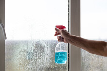 Cleaning Service Came To Clean New House. Hardworking Caucasian Man Carefully Clean Window.man Red Gloves Holding Spraying Blue Bottle On Window.Cleaning Windows With Special Rag And Cleaner