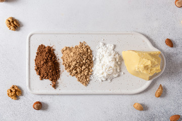 Chocolate organic ingredients: cocoa butter, cocoa powder and coconut sugar on white concrete background with nuts. Chocolatier