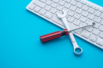 Top view of combination spanner or wrench, screwdriver and keyboard computer on blue background with copy space. Online live support, customer care, after sales service and maintenance concept.