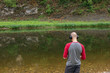 © Olya - Rear view of bald young man standing on river bank and listening to music in headphones. Far from big city bustle. Relaxing outdoors. Melomaniac