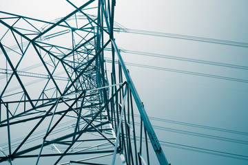 Abstract pattern from bottom view of high voltage pole power transmission tower with clear sky sunny day background in monochrome tone. Green energy, environmental conservation concept.