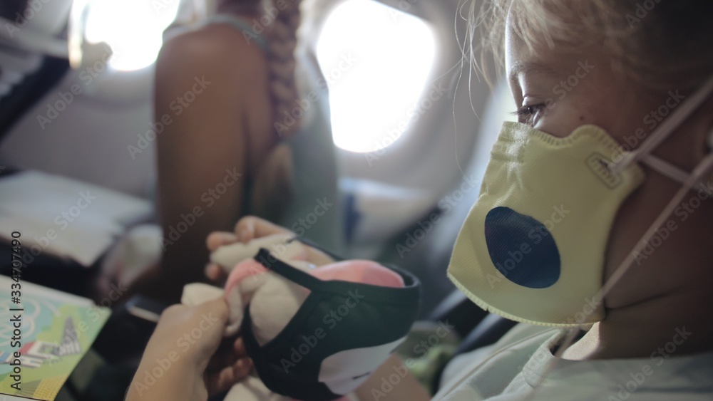 Little girl caucasian at plane with wearing protective medical mask. Child baby tourist at aircraft with respirator play and paint. Coronavirus epidemic sars-cov-2 covid-19 2019-ncov. - obrazy, fototapety, plakaty 