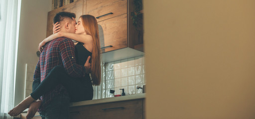 Caucasian girl with red hair and freckles is ebracing her lover in the kitchen