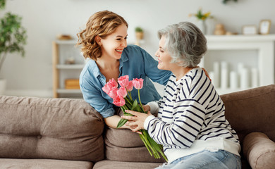Wall Mural - young woman giving flowers to senior mother.