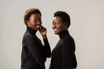 Wall Mural - smiling african american girls in black turtlenecks isolated on grey