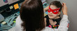 © David Pereiras - Top view of woman teleworking and putting the costume mask on her daughter