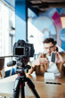 © LIGHTFIELD STUDIOS - Selective focus of blogger in front of digital camera presenting smartphone in coworking space