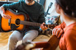 © beavera - Unrecognizable guitar teacher explaining a music class to female student. Woman learning an instrument at home. Music course online concept. Indoor leisure lifestyle for young people.