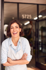 Sticker - Portrait Of Smiling Female Owner Of Florists Standing In Doorway Surrounded By Plants