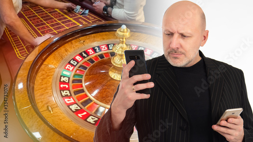 Game in online casino via phone. Concept is a casino application for a mobile phone. Distant gambling. Man on the background of the casino. Table with a tape measure in the background. Roulette Drum