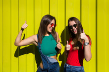 Two Young Best Female Friends Standing By The Yellow Wall