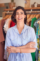 Sticker - Portrait Of Smiling Female Owner Of Fashion Store Standing In Front Of Clothing On Rails