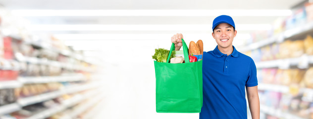 Smiling handsome Asian man holding grocery shopping bag in supermarket banner background with copy spce for food delivery service concept