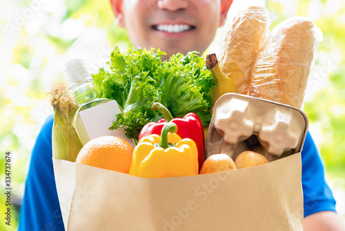Cuadros en Lienzo Smiling delivery man holding a grocery bag ready to deliver to the customer at h