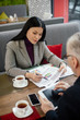 © LIGHTFIELD STUDIOS - selective focus of asian businesswoman talking with businessman and pointing at papers in cafe