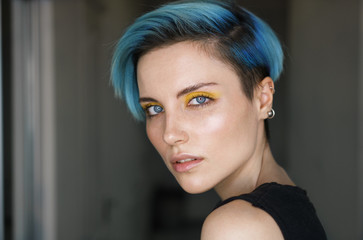 Portrait af a girl with blue hair and yellow eye makeup in a beauty salon in front of a ring light on blue shiny background. Horizontal shot. Close-up