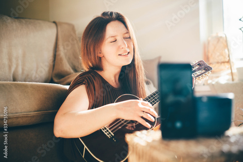 Fotografía Woman singing with ukulele and using phone doing live streaming at home