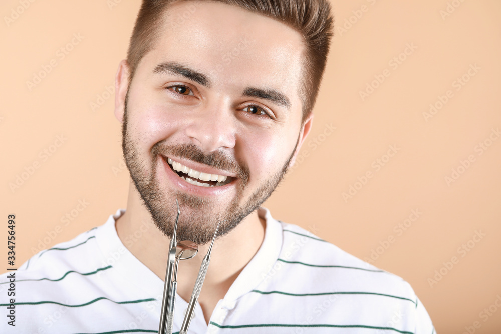 Happy smiling young man with dentist's tools on color background