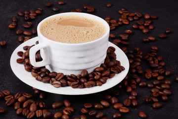 A cup of hot coffee and coffee beans on a black background