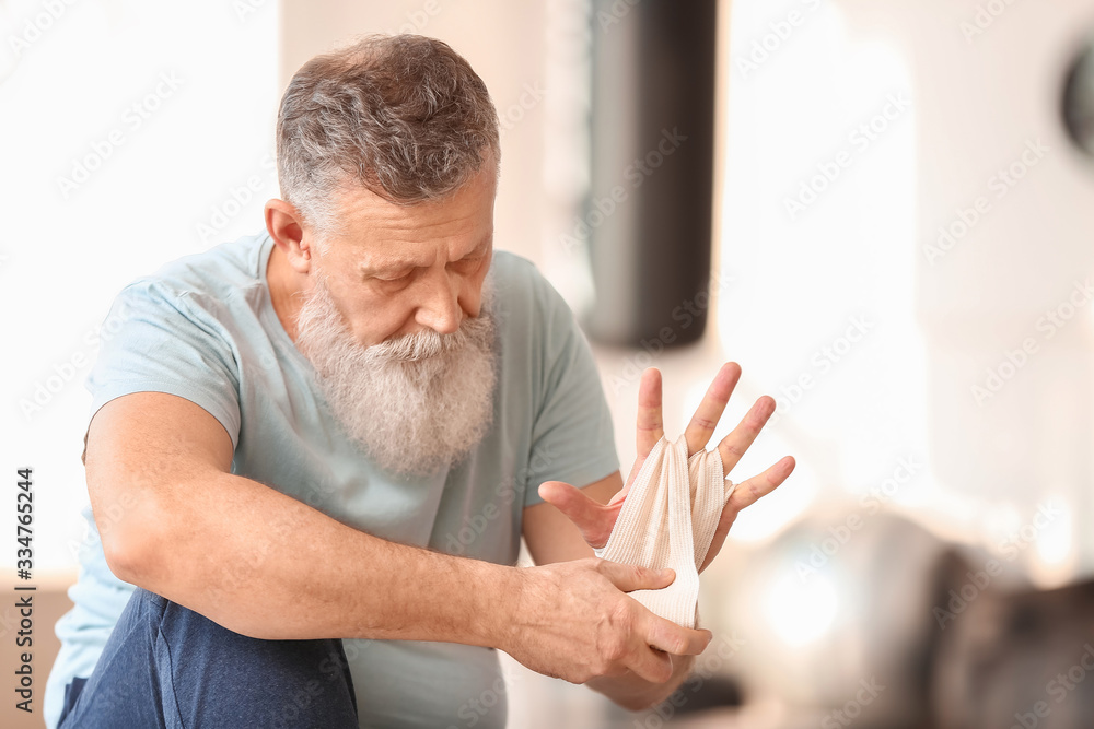 Sporty elderly man applying wrist bands in gym