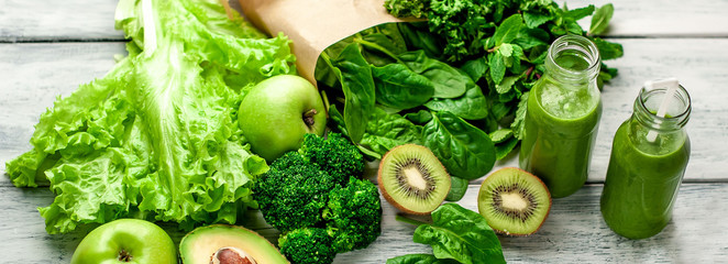  two green healthy smoothies made from apples, spinach, avocado, salad, kiwi on a wood background