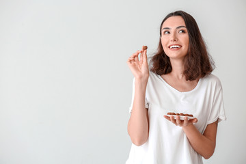 Wall Mural - Beautiful young woman eating tasty chocolate candies on white background