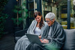 © bnenin - Family time. Mother and daughter looking at laptop at modern home garden, while sitting covered in blankets.
