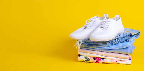 Wall Mural - Stack folded colorful clothing summer and white sneakers on yellow background