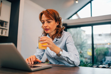 Poster - Close-up portrait of a businesswoman drinking juice and using laptop.