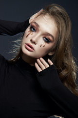 Wall Mural - Beauty portrait blonde woman with makeup and big blue eyes, natural cosmetics, clean delicate skin of the girl face, black clothes. Drops of makeup trickle from the girl eyes