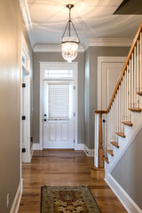 View of a white front door entrance in a new construction house with a hanging chandelier clear glass light and a staircase