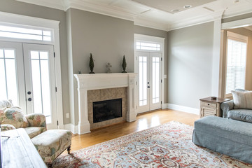 a bright and airy neutral beige living room den in a new construction house with a white and tiled fireplace as the main focal point as well as a decorative rug and lots of natural window light.