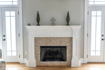 a bright and airy neutral beige living room den in a new construction house with a white and tiled fireplace as the main focal point as well as a decorative rug and lots of natural window light.