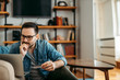 © bnenin - Charming man sitting on floor at home, holding credit card and looking at laptop, portrait.