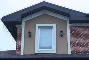 Sticker - one white window on the brown wall of the attic of a private house against a gray sky