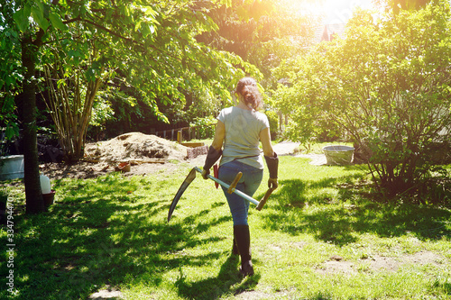 Fotomural Woman at gardening in the garden mows wild meadow with scythe on a sunny summer