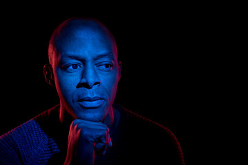 Black man with blue and red light, isolated on black background, looking sideways. Uncertainty expression.