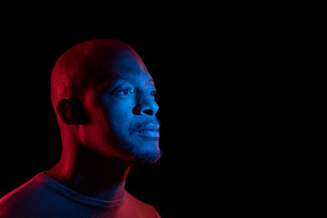 Black man with blue and red light, isolated on black background, looking sideways. Copyspace