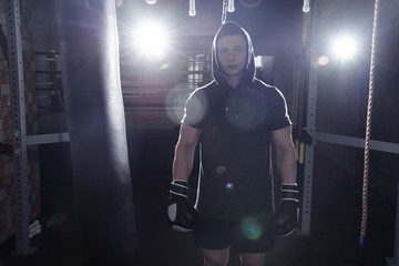 Wall Mural - Professional boxer muscular man beats a punching bag in boxing gloves, training an athlete in the gym, an aggressive battle in dark colors