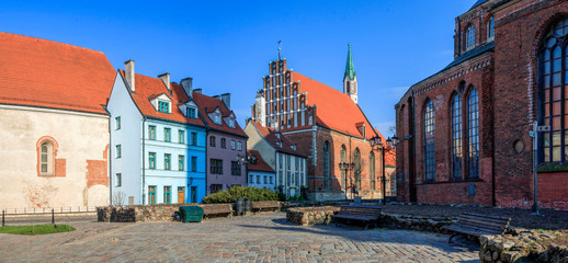 Wall Mural - Old town square with beautiful St. John's Church and cute red roofed houses in Riga, Latvia