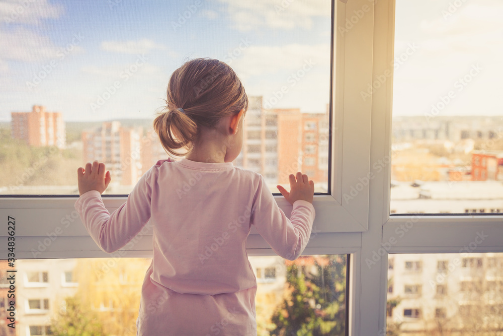 Little girl looking outside through the window - obrazy, fototapety, plakaty 