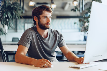 Wall Mural - Bearded man freelancer using computer in a modern coworking place. Freelance business concept